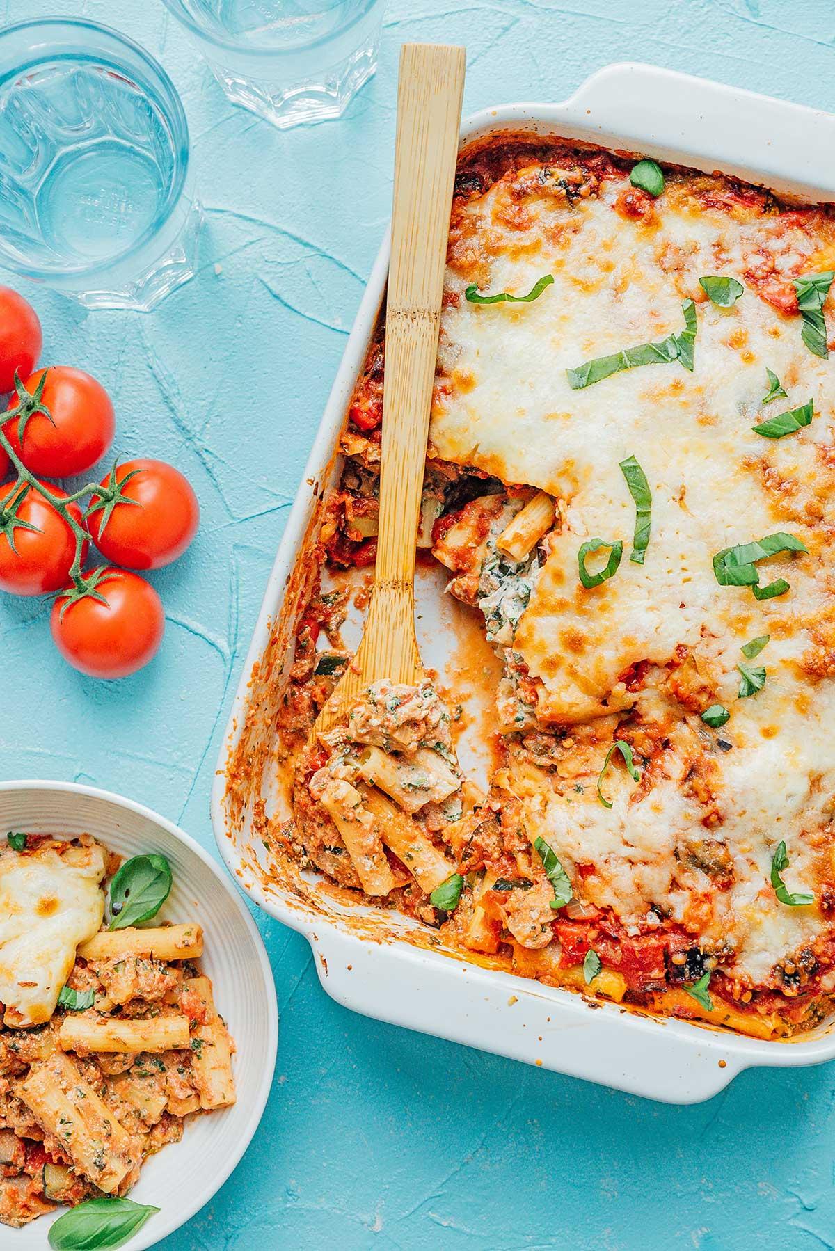 Eine Portion gebackenes Ziti in einer Schüssel neben einer Auflaufform, gefüllt mit gebackenem Ziti