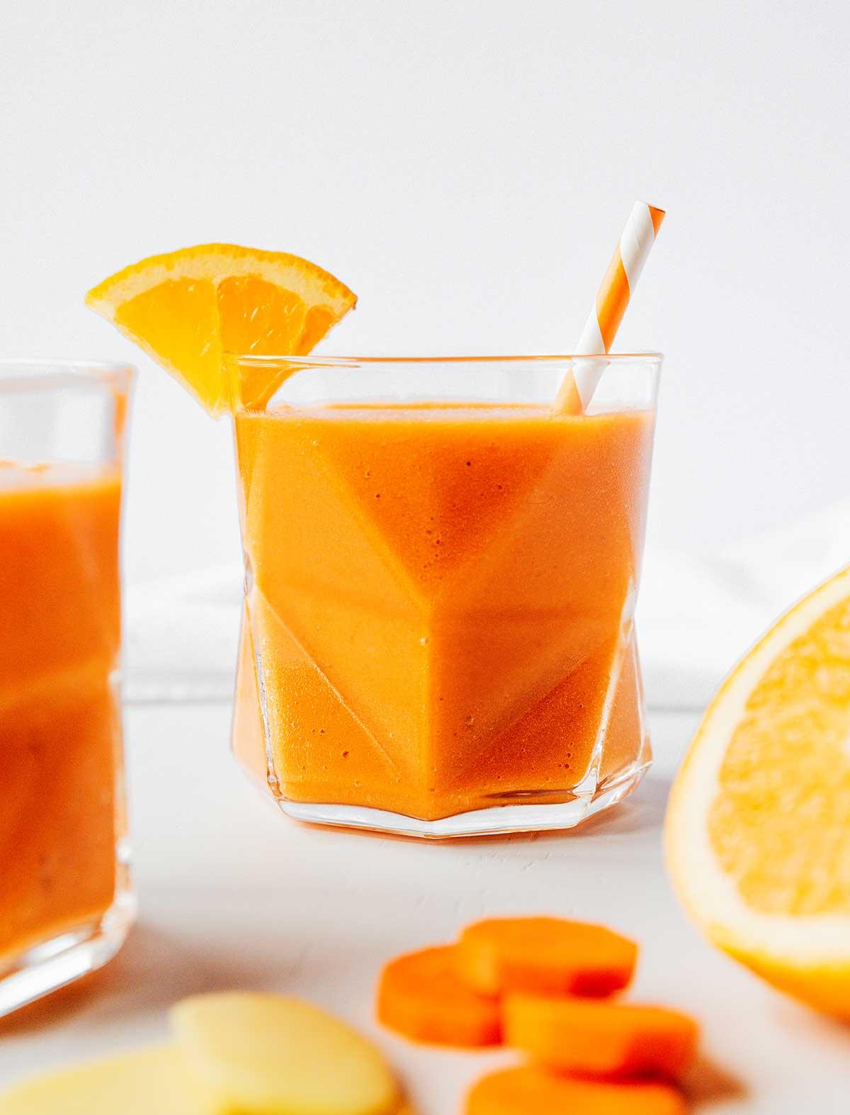 Karotten-Ingwer-Smoothie 2 Ein Glas gefüllt mit frisch gemischtem Karotten-Smoothie mit Zitrusfrüchten und Ingwer, garniert mit einer Orangenscheibe