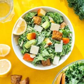 Grünkohlsalat mit Äpfeln und Avocado in einer Schüssel auf gelbem Hintergrund.