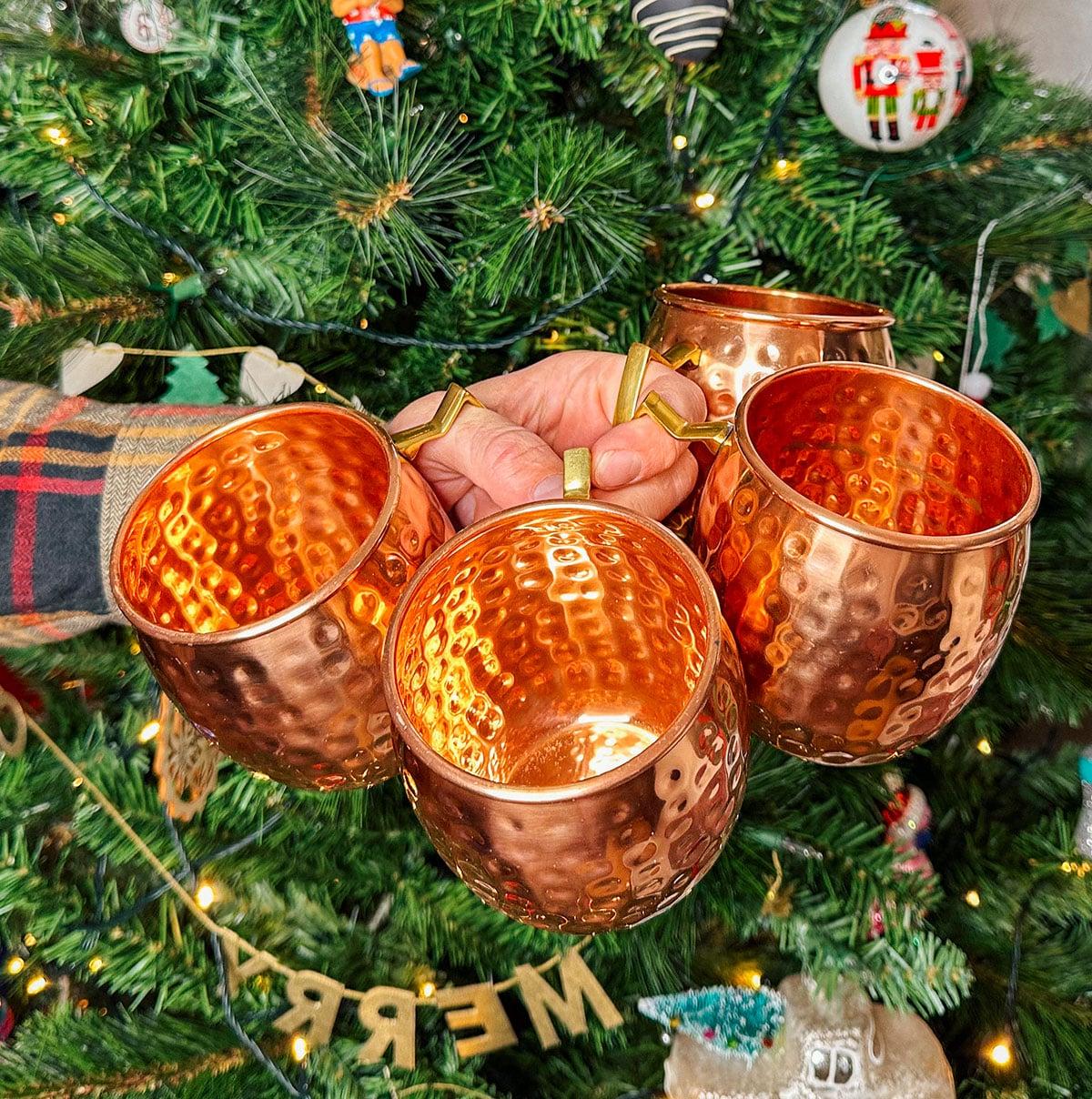 47 Geschenkideen für Feinschmecker 20 Kupferbecher für Moscow Mule als Geschenk vor einem Weihnachtsbaum.