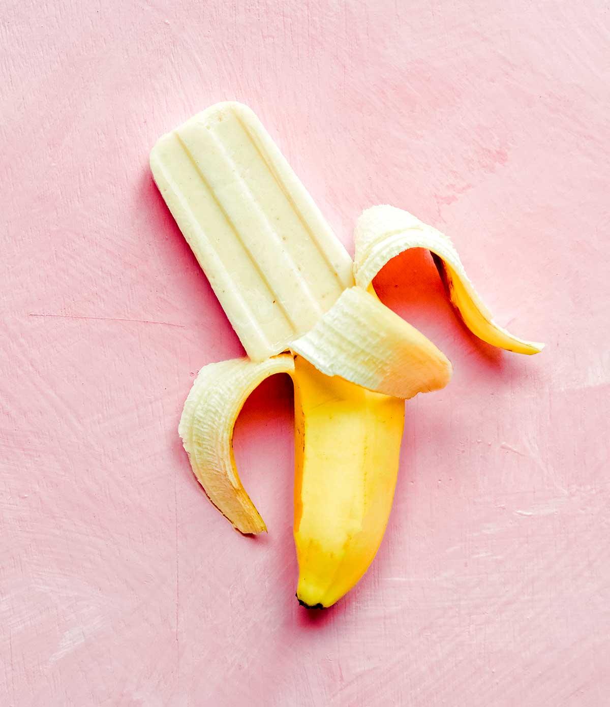 Ein Bananen-Popsicle kommt auf einer Bananenschale auf einem pinkfarbenen Hintergrund hervor.