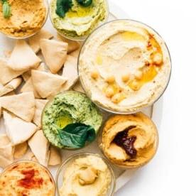 Schüssel mit Regenbogen-Hummus-Sorten auf weißem Hintergrund.