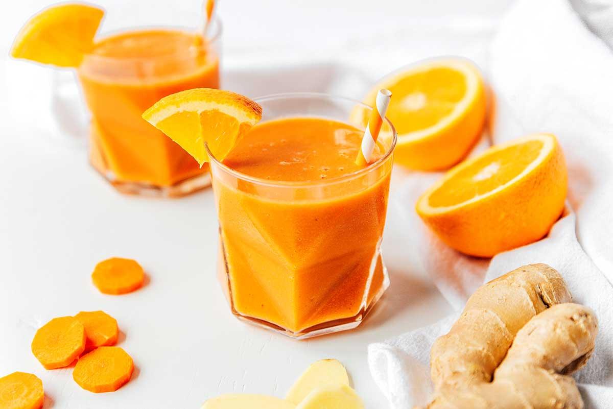 Karotten-Ingwer-Smoothie 3 Ein Glas gefüllt mit frisch gemischtem Karotten-Smoothie mit Zitrusfrüchten und Ingwer, garniert mit einer Orangenscheibe