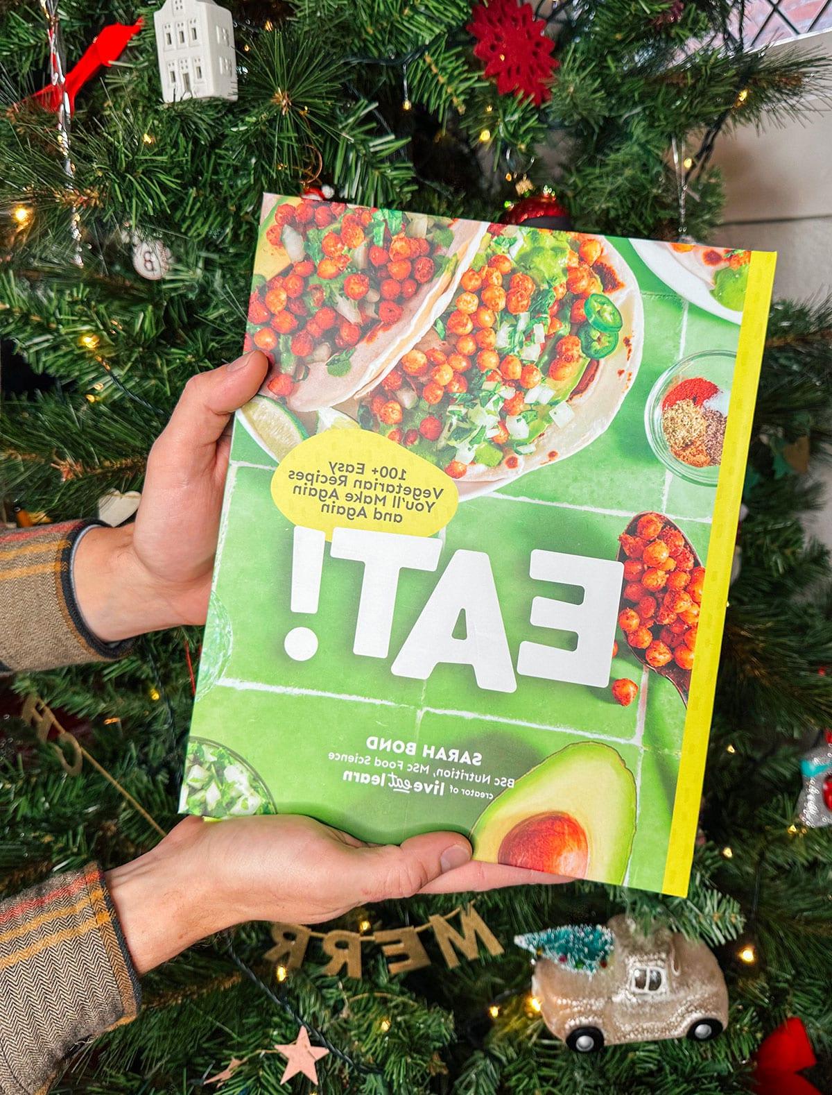 47 Geschenkideen für Feinschmecker 22 Mein vegetarisches Kochbuch 'Eat!' als Geschenk vor einem Weihnachtsbaum.