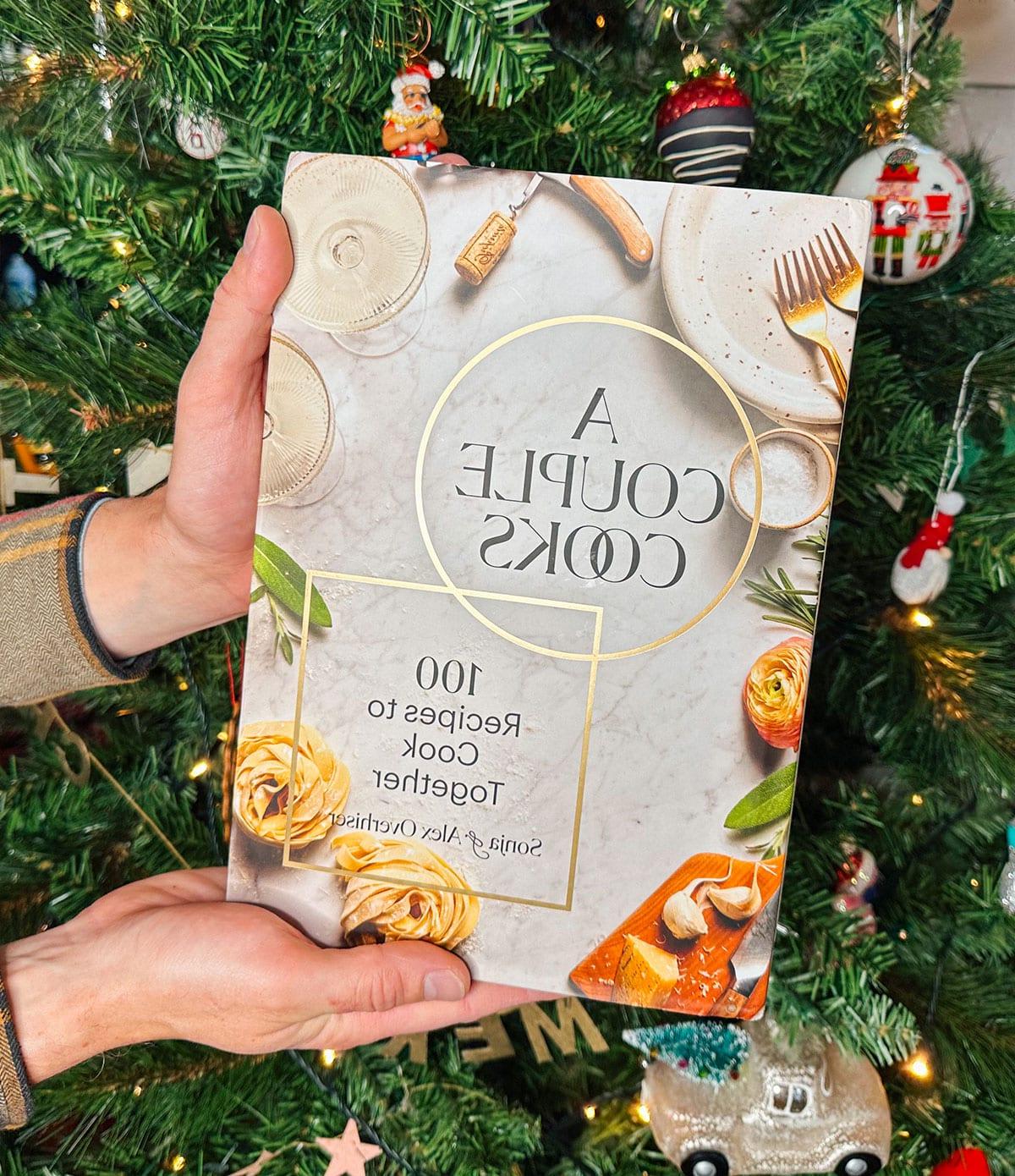 47 Geschenkideen für Feinschmecker 24 Das Kochbuch 'A Couple Cooks' als Geschenk vor einem Weihnachtsbaum.