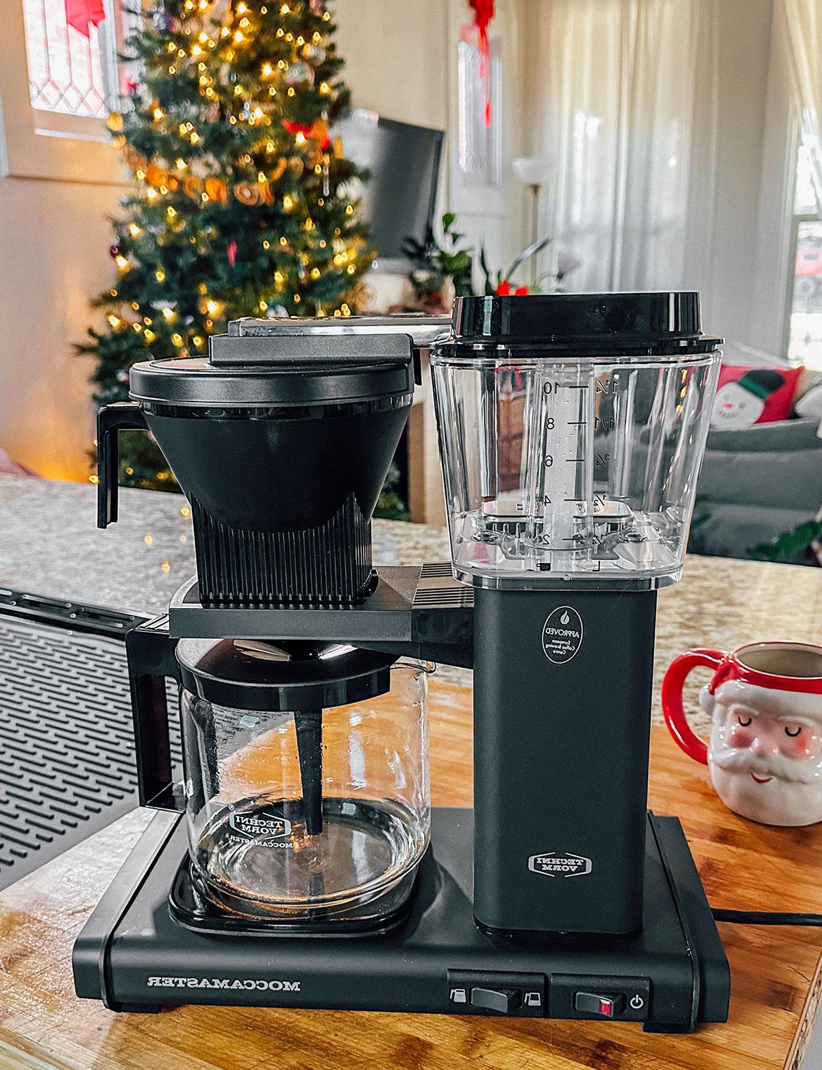 47 Geschenkideen für Feinschmecker 26 Eine Moccamaster Kaffeemaschine als Geschenk vor einem Weihnachtsbaum.