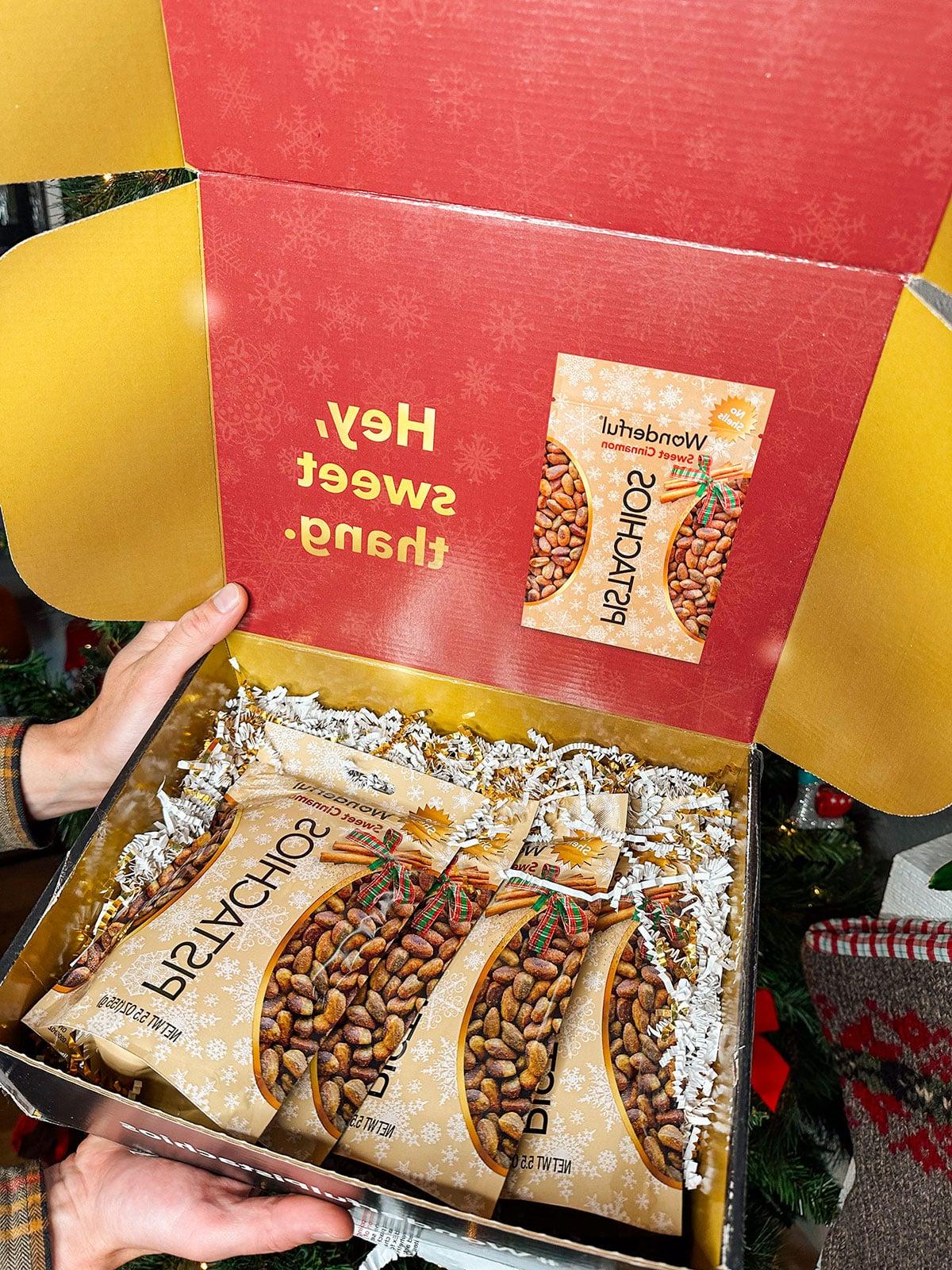 47 Geschenkideen für Feinschmecker 30 Hand hält eine Tüte Wonderful Pistazien vor einem Weihnachtsbaum.