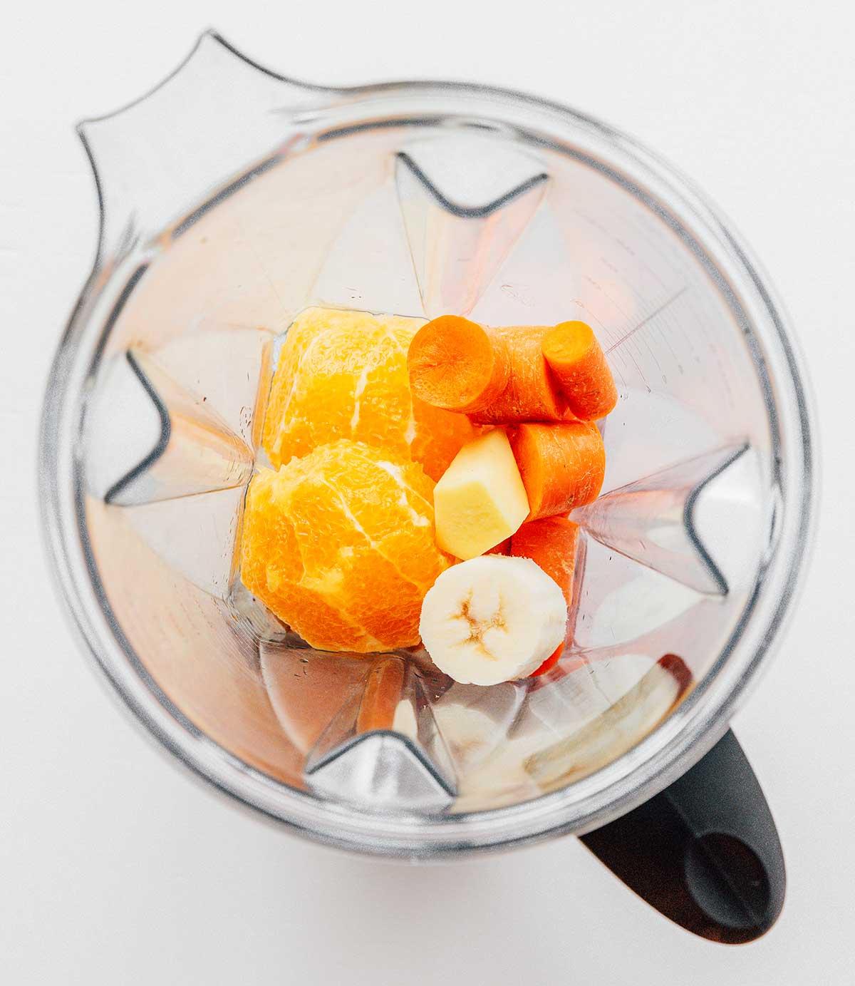 Karotten-Ingwer-Smoothie 4 Ein Mixer gefüllt mit geschnittenen Bananen, geschnittenen Karotten, gehackter Ananas und 2 Hälften einer Orange