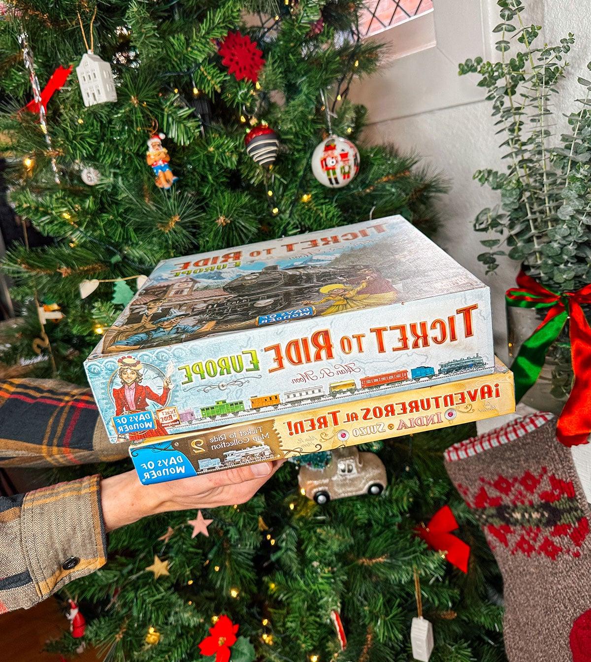 47 Geschenkideen für Feinschmecker 33 Brettspiele wie Ticket To Ride und Telestrations als Geschenk vor einem Weihnachtsbaum.