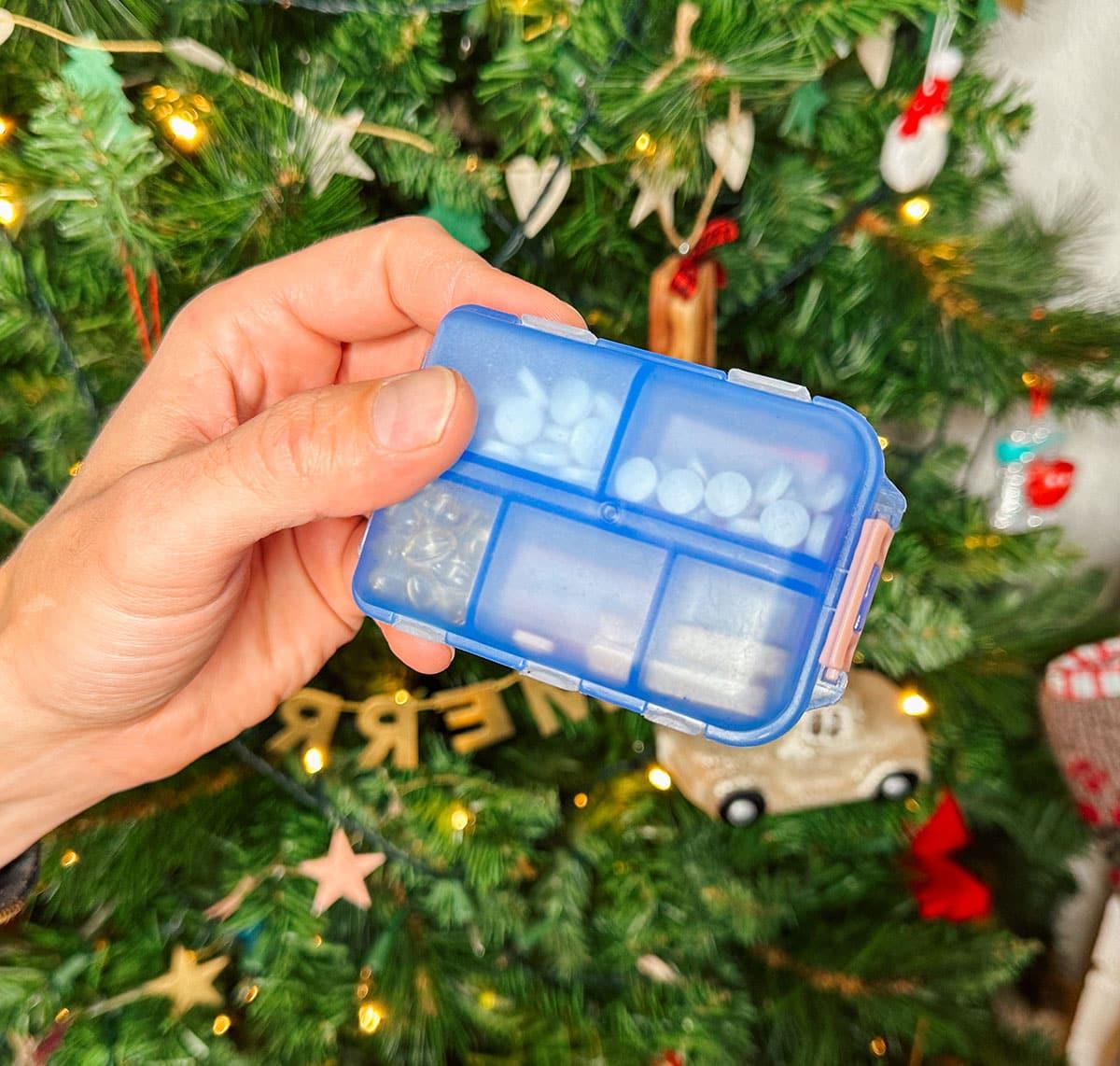 47 Geschenkideen für Feinschmecker 35 Eine kleine Reise-Pillendose als Geschenk vor einem Weihnachtsbaum.