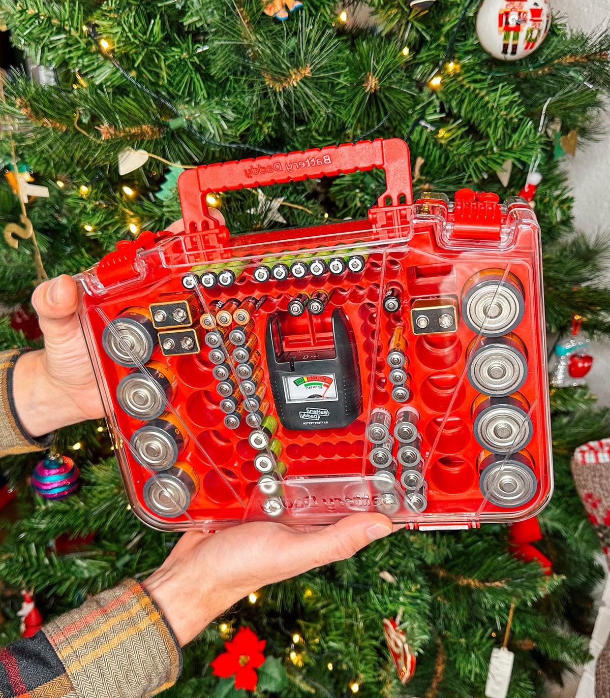 47 Geschenkideen für Feinschmecker 36 Ein Battery Daddy Batterie-Organizer als Geschenk vor einem Weihnachtsbaum.