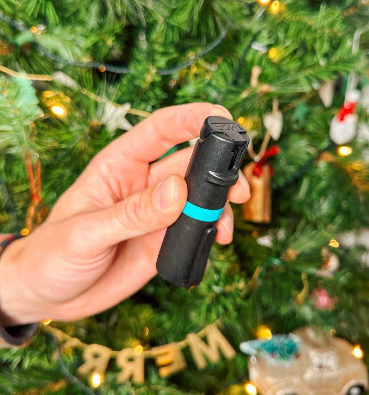 47 Geschenkideen für Feinschmecker 41 Pfefferspray als praktisches Geschenk vor einem Weihnachtsbaum.