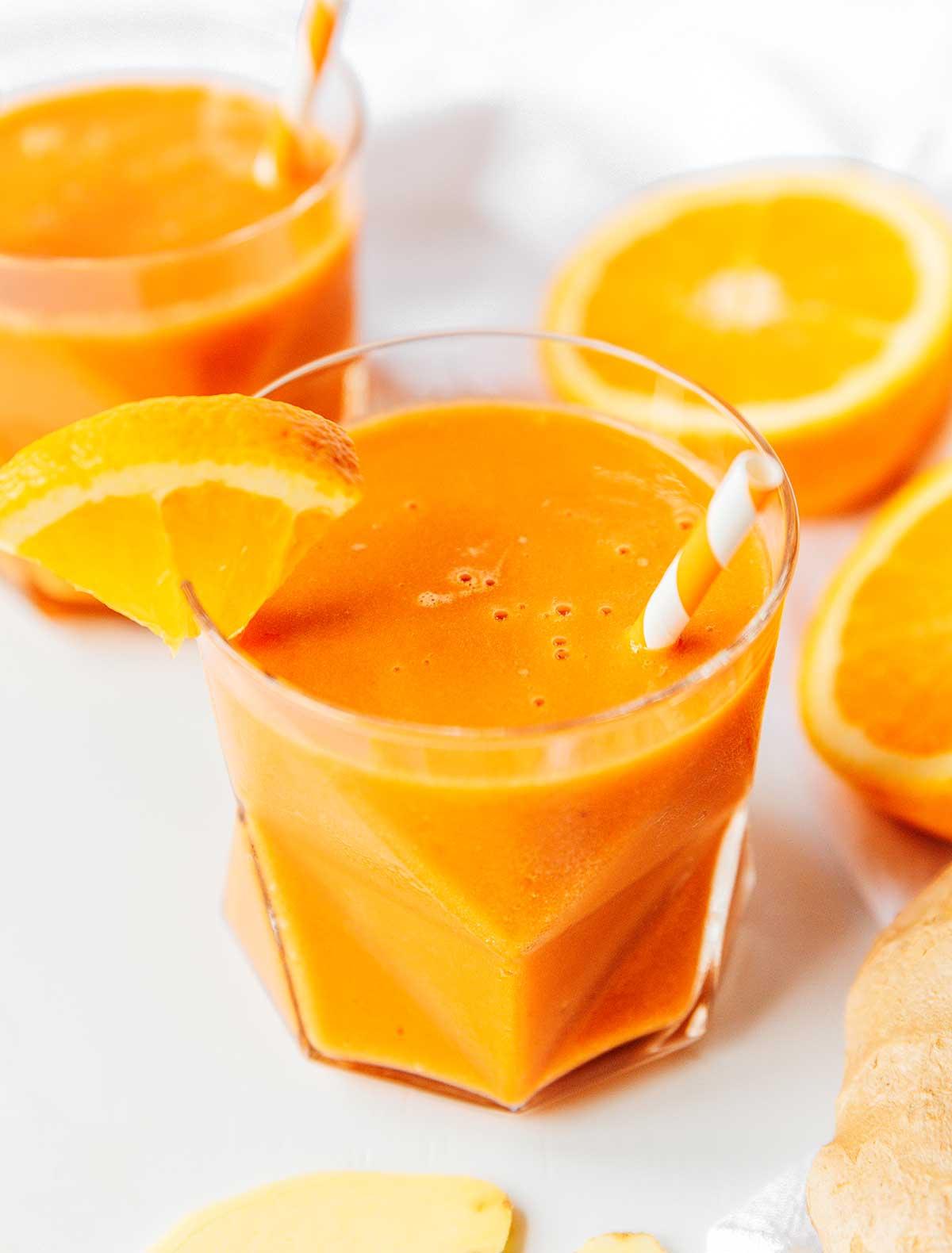 Karotten-Ingwer-Smoothie 7 Ein Glas gefüllt mit frisch gemischtem Karotten-Smoothie mit Zitrusfrüchten und Ingwer, garniert mit einer Orangenscheibe