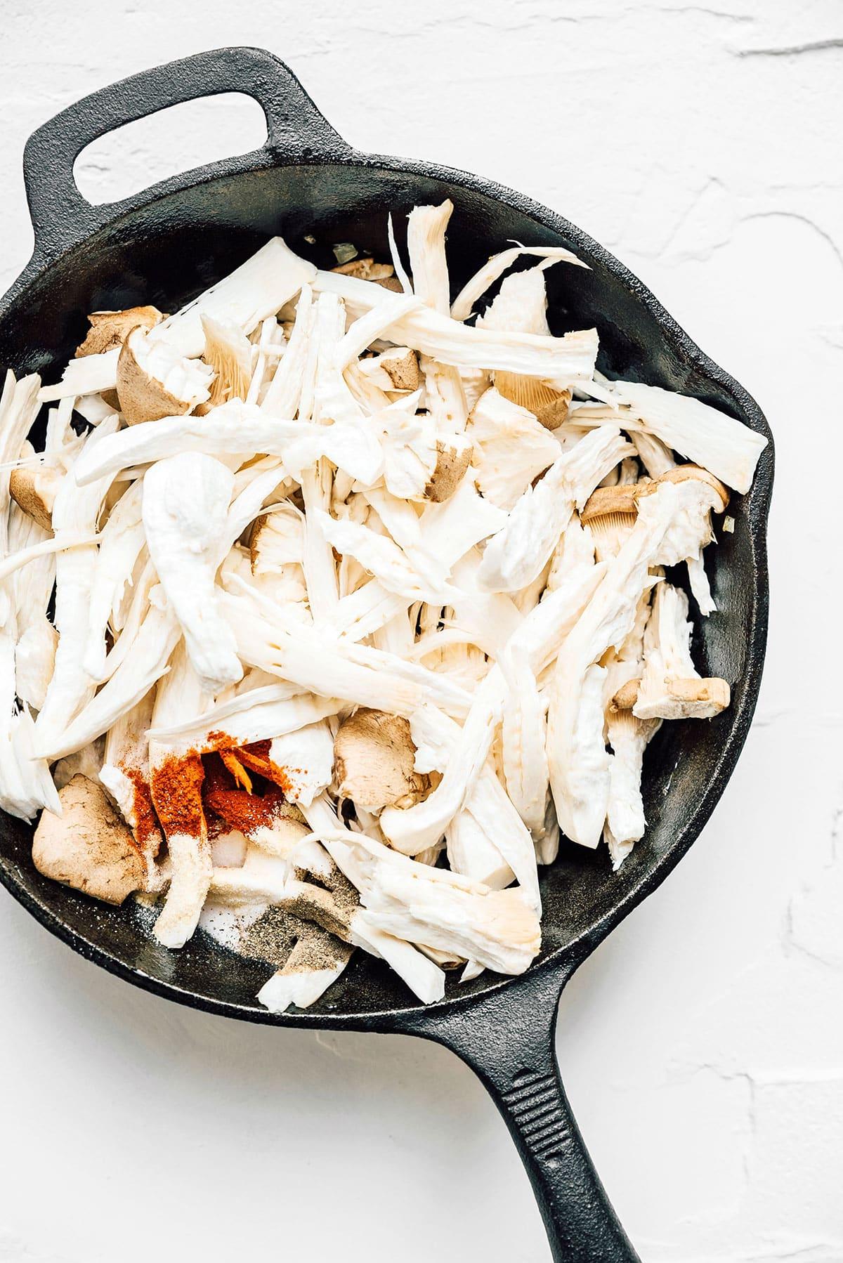 Vegetarisches Philly Cheesesteak mit zerzupften Pilzen 7 Zerzupfte Austernpilze werden in einer gusseisernen Pfanne angebraten.