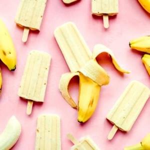 Bananen-Popsicles und ganze Bananen bilden ein spielerisches Muster auf einem leuchtend pinken Hintergrund.