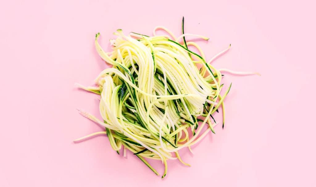Zucchininudeln zubereiten 10 Ein Stapel Engelshaar-Zucchini-Nudeln auf rosafarbenem Hintergrund.