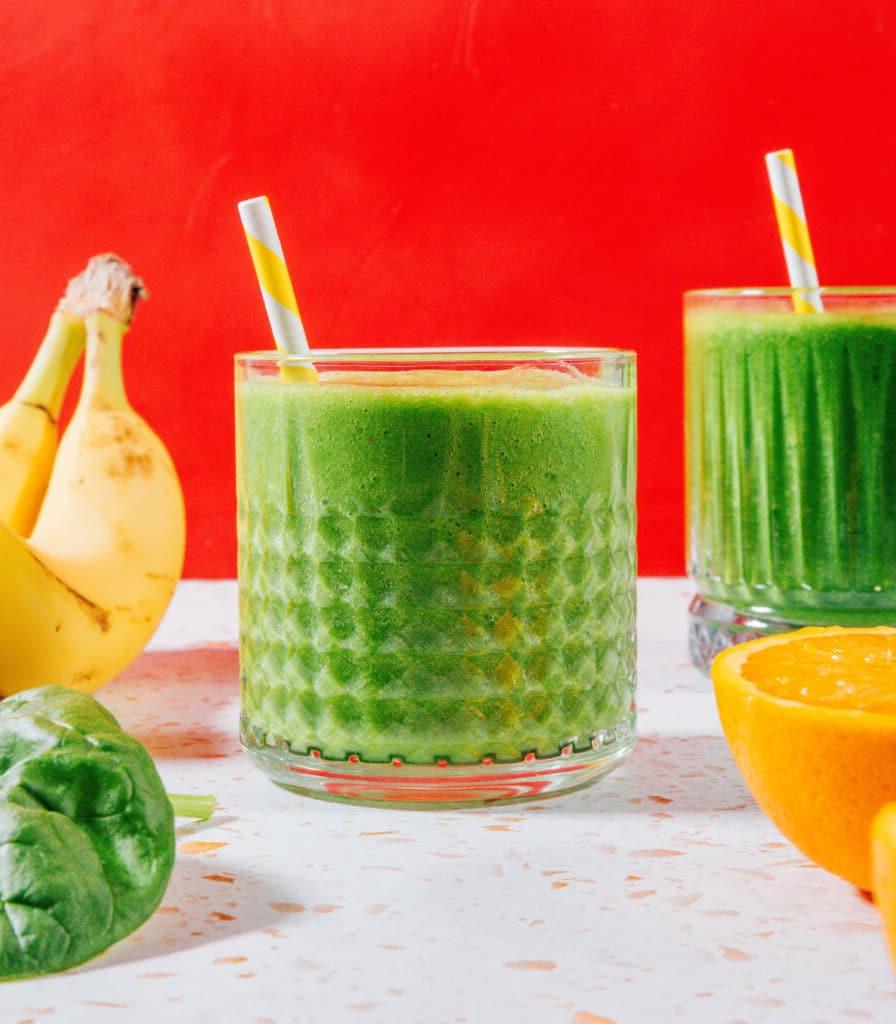 Grüner Smoothie in einem Glas mit rotem Hintergrund.