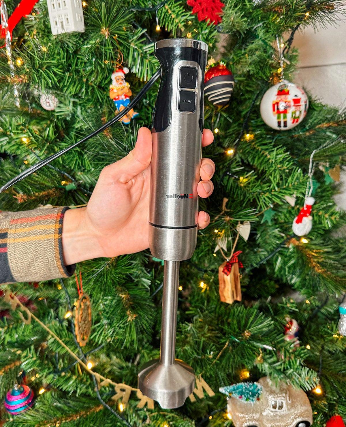 47 Geschenkideen für Feinschmecker 10 Ein praktischer Stabmixer als Geschenk vor einem Weihnachtsbaum.