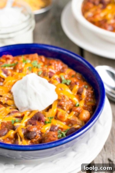 A steaming bowl of homemade three bean beef chili, garnished with a dollop of sour cream and shredded cheddar cheese, ready to be enjoyed.