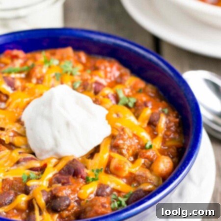 photo of a bowl of big batch three bean chili garnished with a dollop of sour cream and grated cheddar cheese