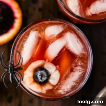 overhead photo of a cup of Halloween punch garnished with eyeballs made of fruit Lychees and blueberries with a fake spider on the rim to look extra spooky