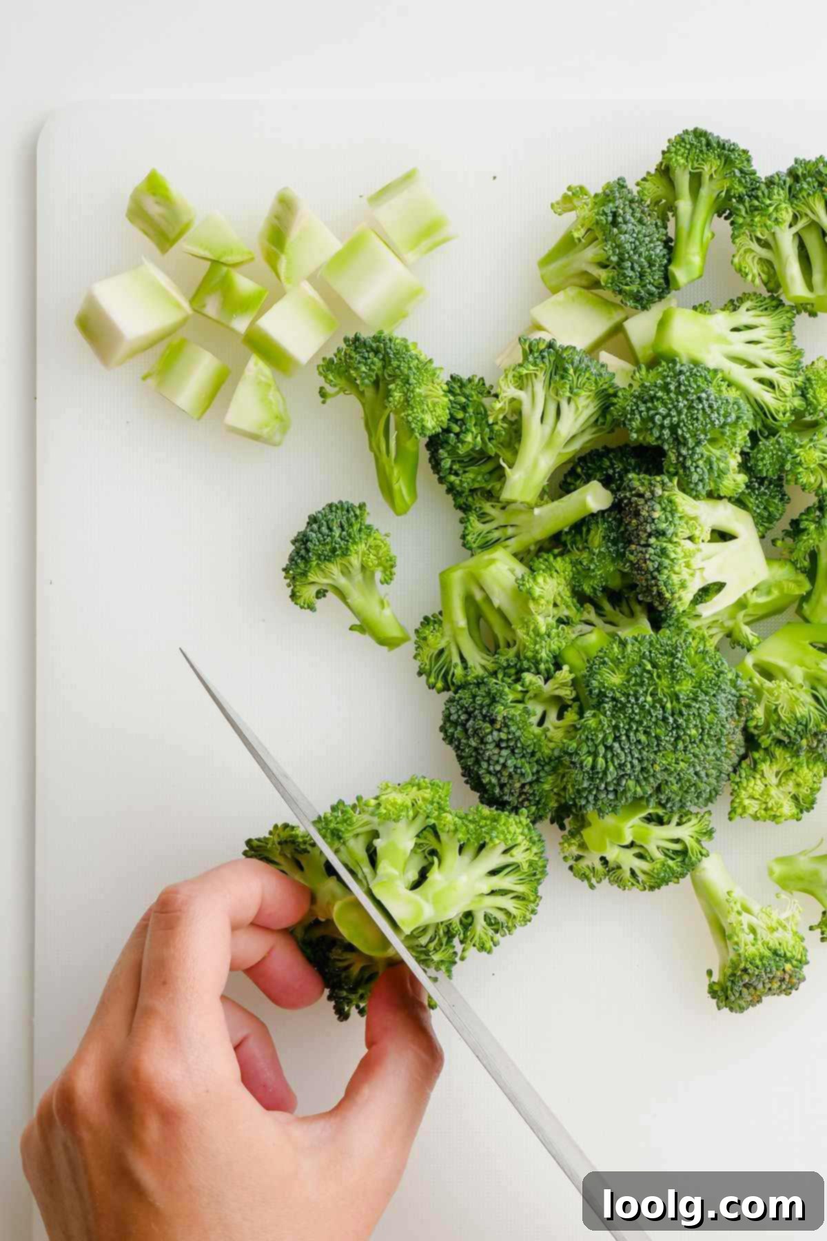 A broccoli floret being expertly cut into smaller, bite-sized pieces on a white cutting board.