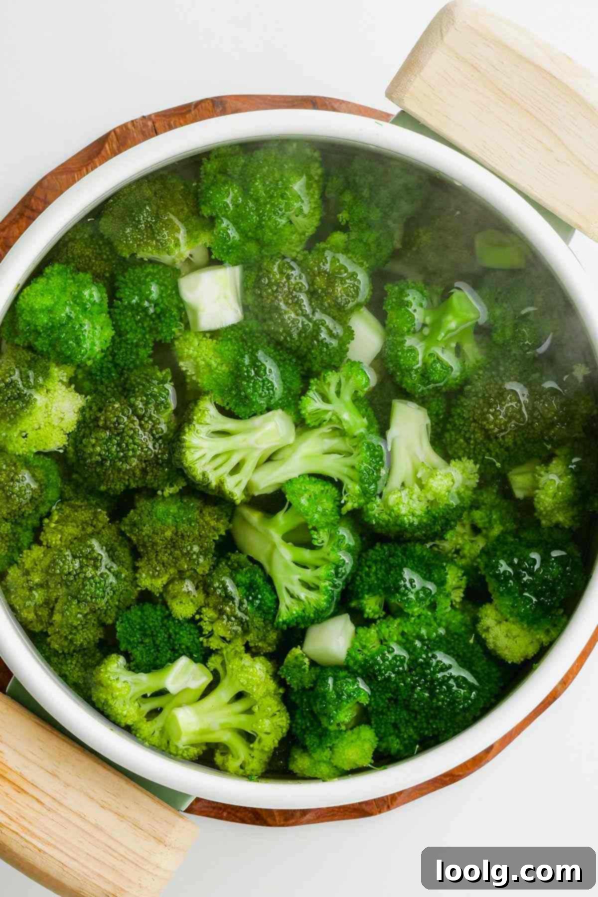 Fresh broccoli florets being gently placed into a pot of rapidly boiling water for blanching.