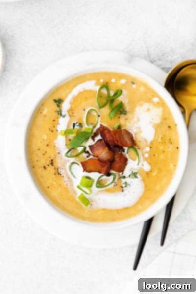 A spoon resting next to a bowl of creamy corn chowder, garnished with fresh herbs and bacon bits