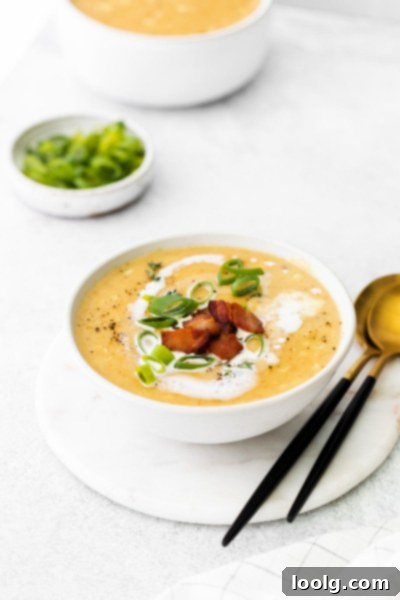 A full bowl of creamy corn chowder with a spoon, garnished with green onions and bacon bits, ready to eat