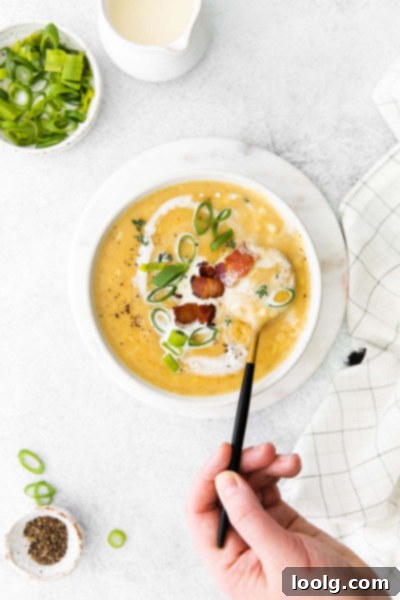 Overhead shot of a bowl of creamy corn chowder garnished with fresh herbs and bacon, inviting to eat