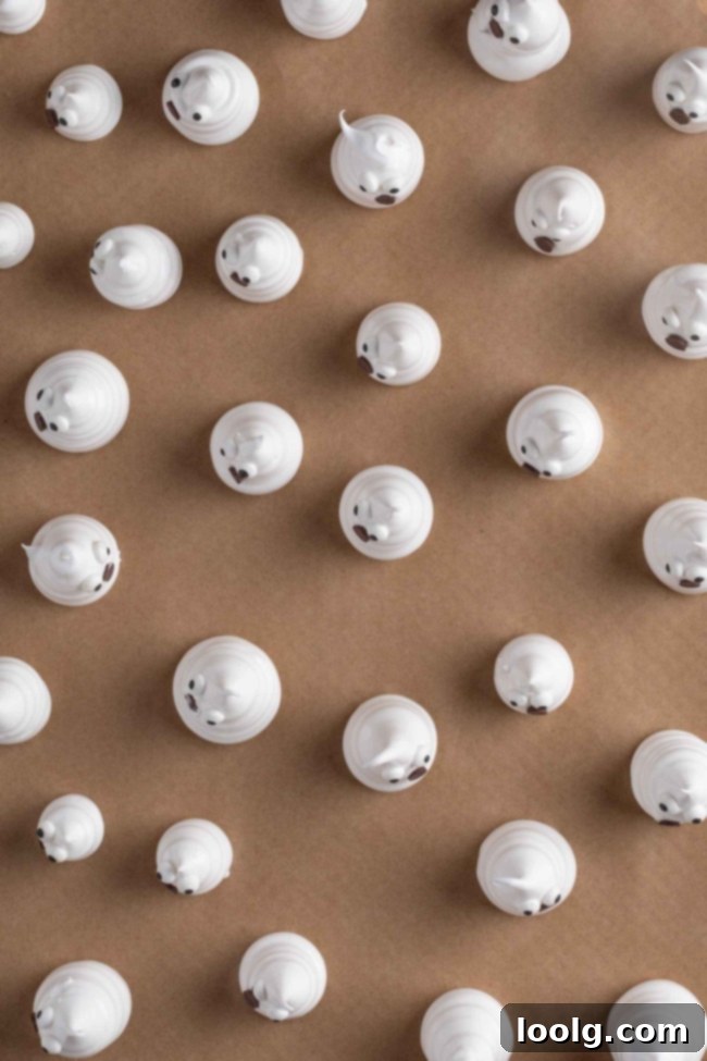 Several piped meringue ghosts on a baking sheet, showing slight variations in size and shape.