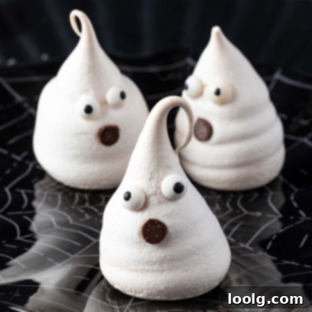 A plate of perfectly baked Meringue Ghosts with candy eyes and chocolate chip mouths, ready to be served for Halloween.