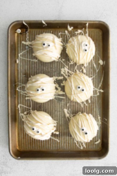 A Halloween Hot Chocolate Bomb being decorated with drizzled white chocolate for a mummy effect.