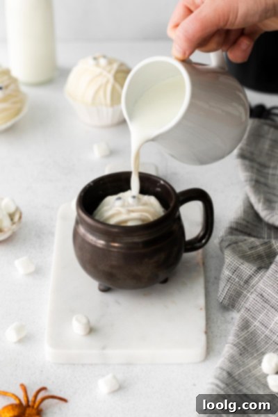 A Halloween Hot Chocolate Bomb melting in a mug of hot milk, releasing marshmallows.