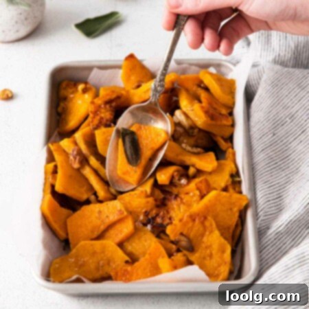 Image of a hand with a serving spoon dipping into a dish of creamy, buttery, nutty baked butternut squash seasoned with fresh sage, garlic cloves and crunchy walnuts
