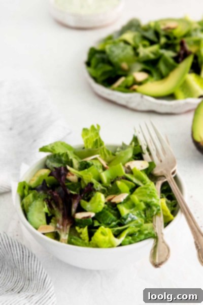 A close-up of a Green Goddess Salad, showcasing the crisp lettuce, bright avocado, cucumber, and snap peas coated in a creamy dressing.