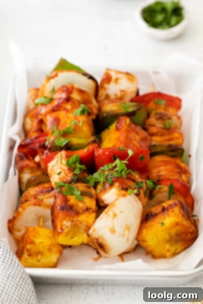 Delicious grilled chicken pineapple kabobs with red and green bell peppers and onion on a white platter, garnished with fresh parsley.