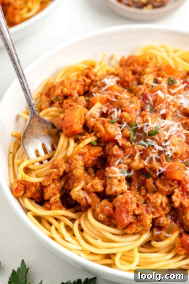 A close-up of a spoon stirring creamy chicken bolognese sauce in a pot, highlighting its texture.