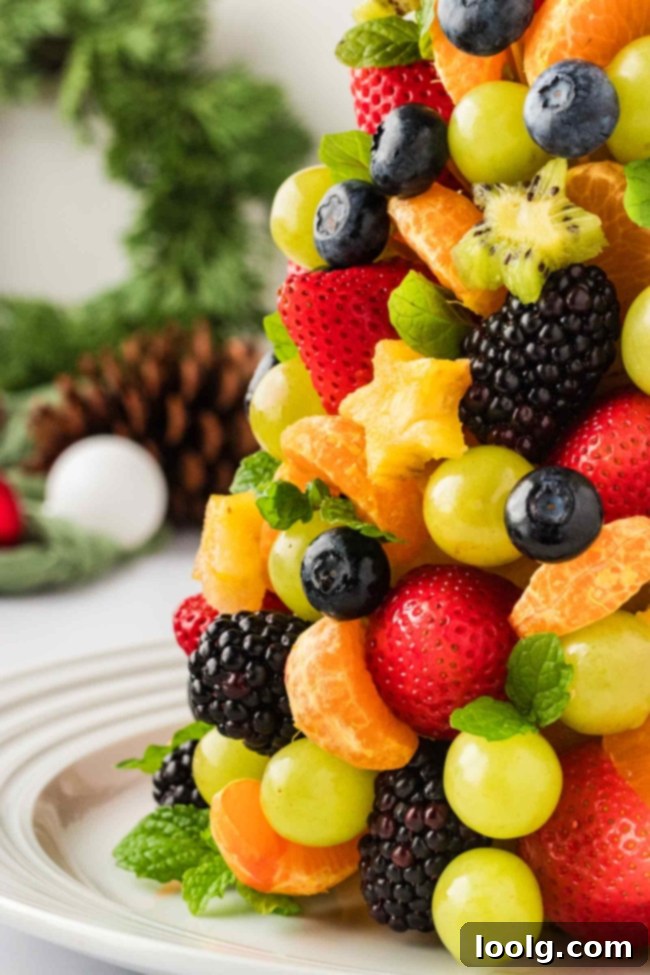 A close-up of various fresh fruits, including strawberries, blueberries, kiwi stars, and mandarin segments, ready to be assembled onto the fruit Christmas tree.