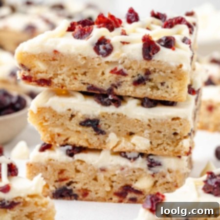 Close-up photo of 3 stacked bliss bars showing the layers of the moist blondie base, topped with a white chocolate cream cheese frosting and topped with dried cranberries and piped white chocolate frosting strips to add another level of texture and goodness.