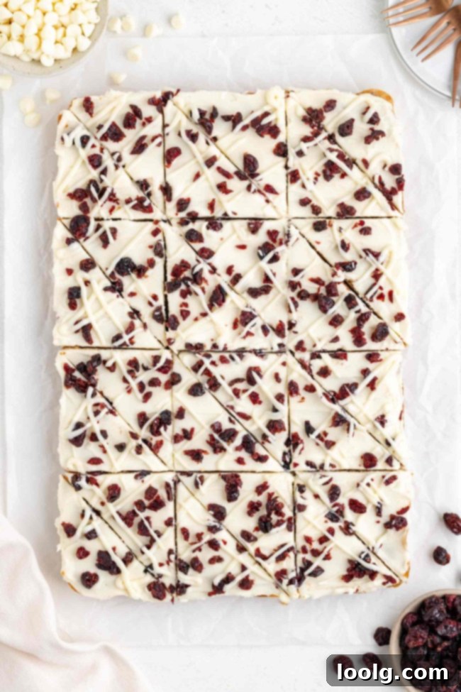 A close up shot of a whole tray of blissful cranberry bars, topped with a white chocolate cream cheese frosting and sprinkled with dried cranberries.