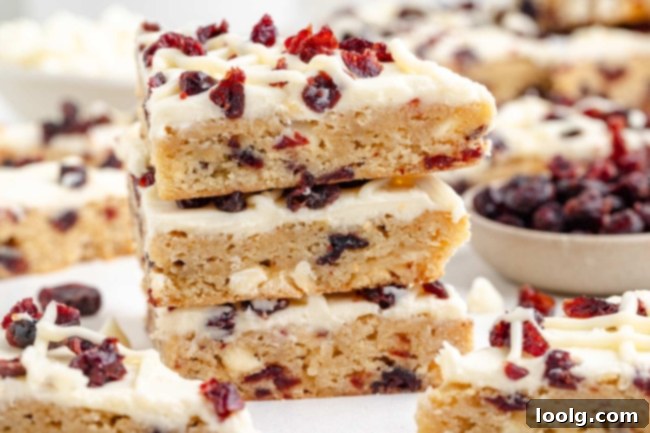 A close up shot of a whole tray of blissful cranberry bars, topped with a white chocolate cream cheese frosting and sprinkled with dried cranberries and piped white chocolate frosting strips.