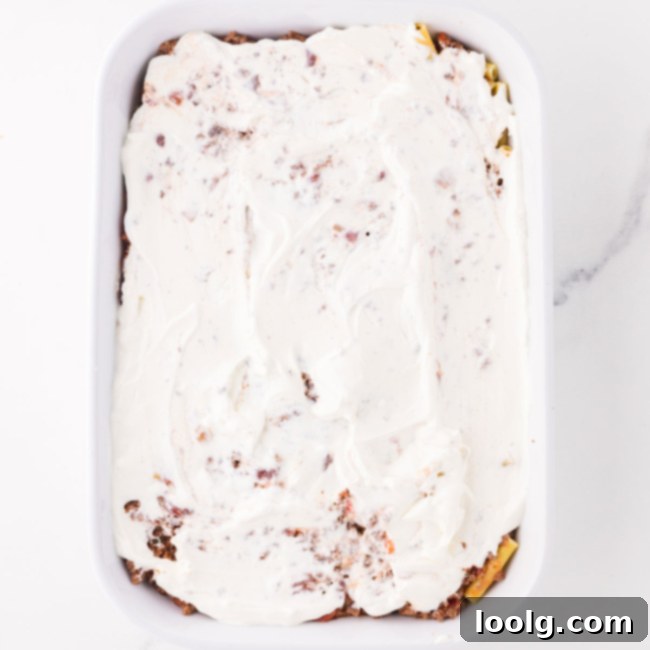 a layer of sour cream being added on top of the sauce layer