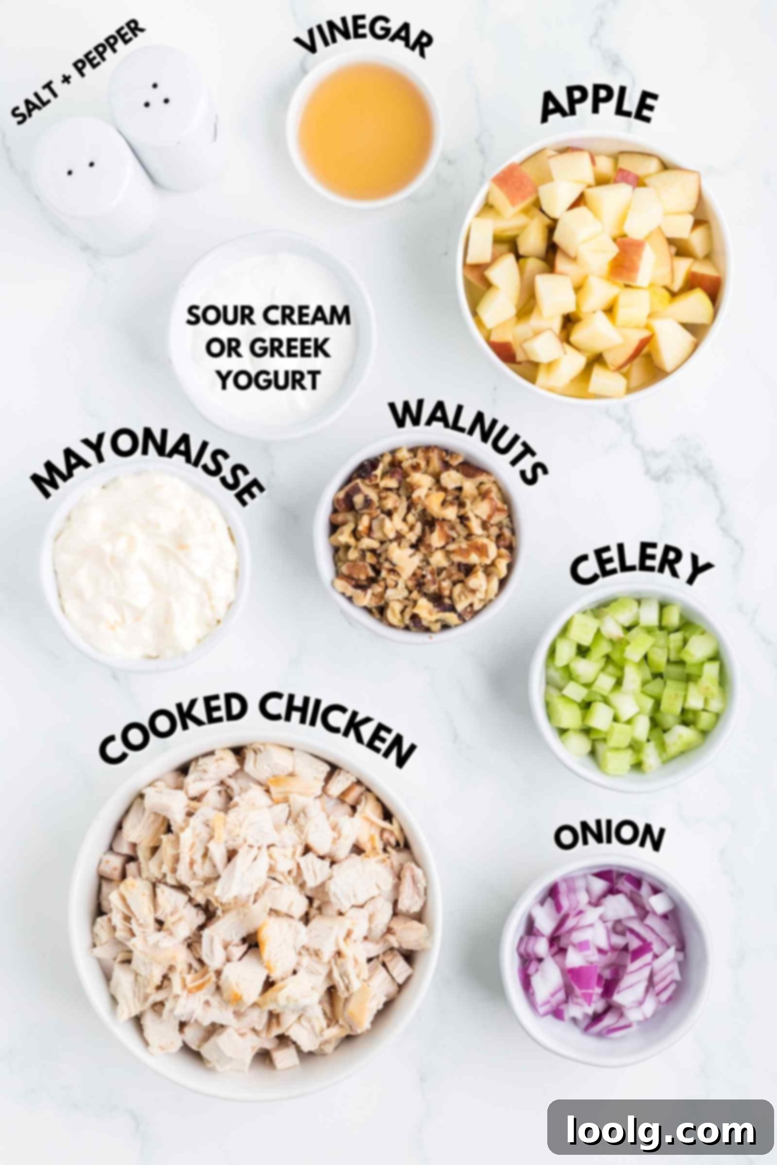 A collection of fresh ingredients laid out on a white surface, ready to be prepared for an apple walnut chicken salad, including chicken, apples, walnuts, and dressing components