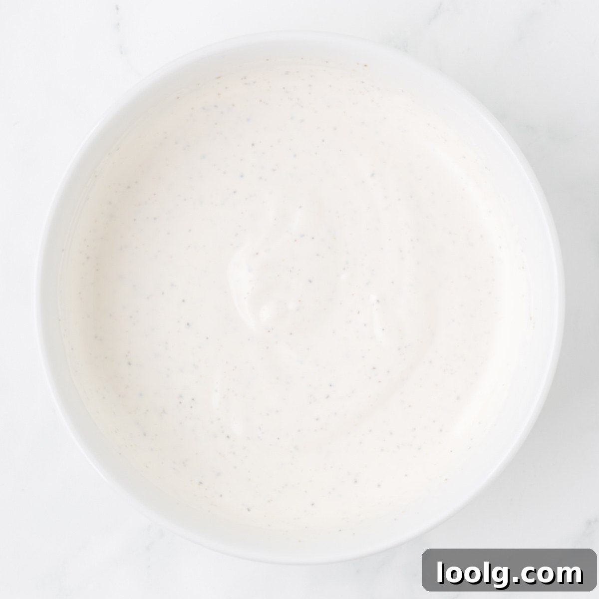 Whisking mayonnaise, sour cream, and apple cider vinegar together in a small white bowl to create a creamy dressing