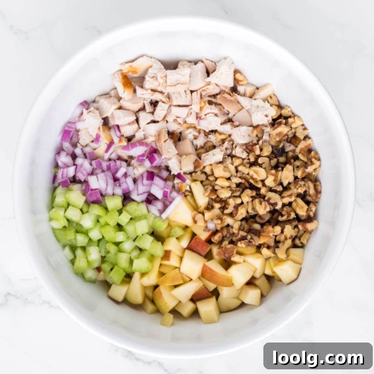 A large mixing bowl filled with diced cooked chicken, chopped apples, toasted walnuts, celery, and red onion, ready for the dressing