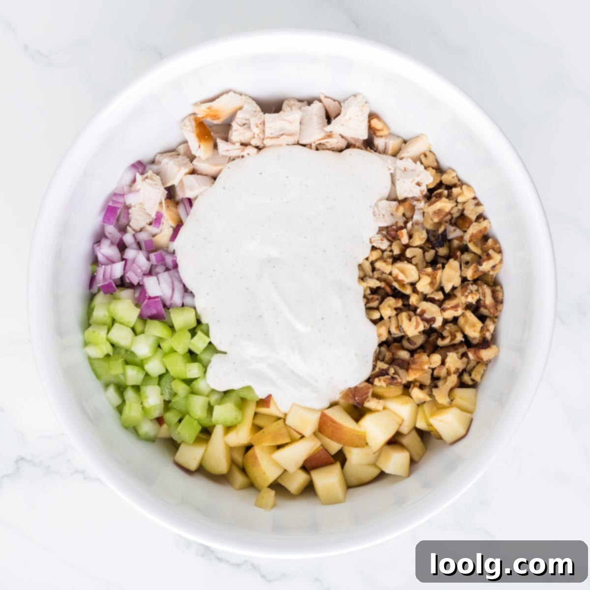 Pouring the creamy dressing over the mixed chicken, apple, and walnut salad ingredients in a large bowl
