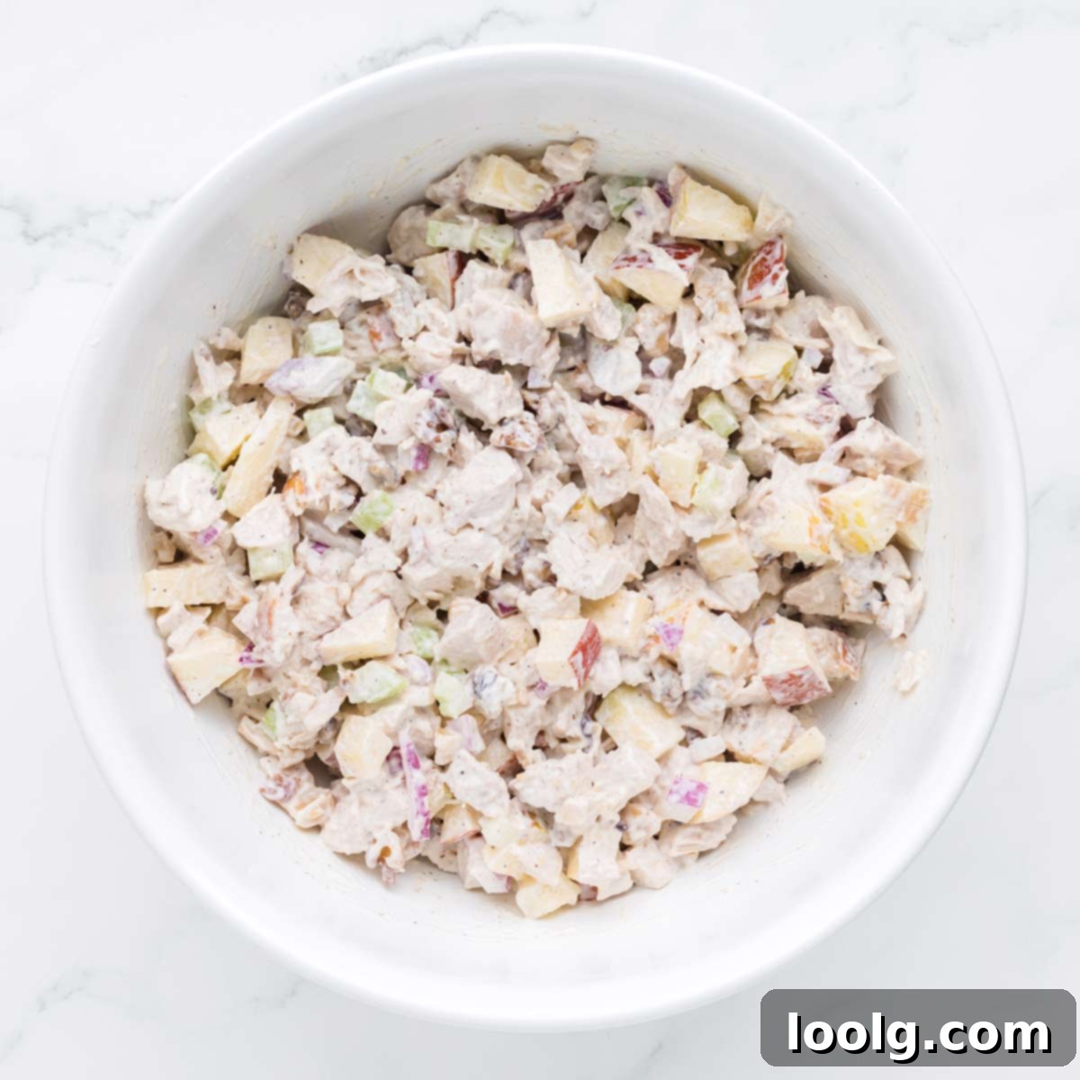 A large white bowl filled with the freshly mixed apple walnut chicken salad, ready to be chilled