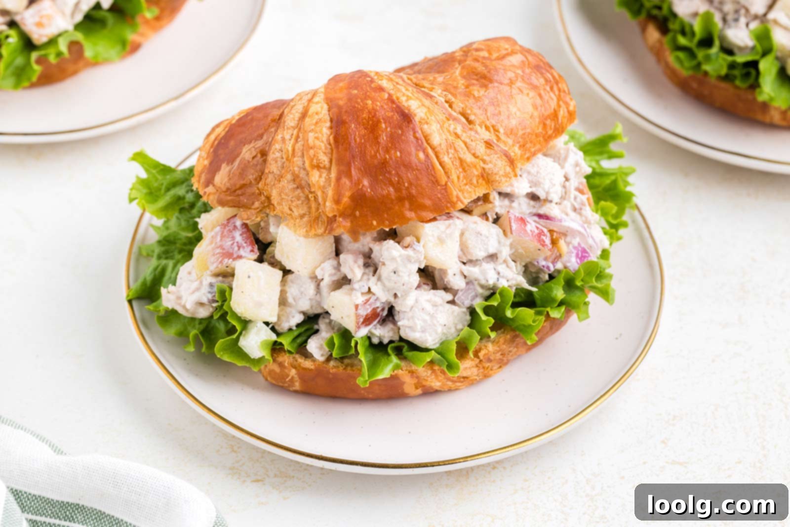 A delicious apple walnut chicken salad sandwich served in a flaky croissant on a white table, ready to be enjoyed