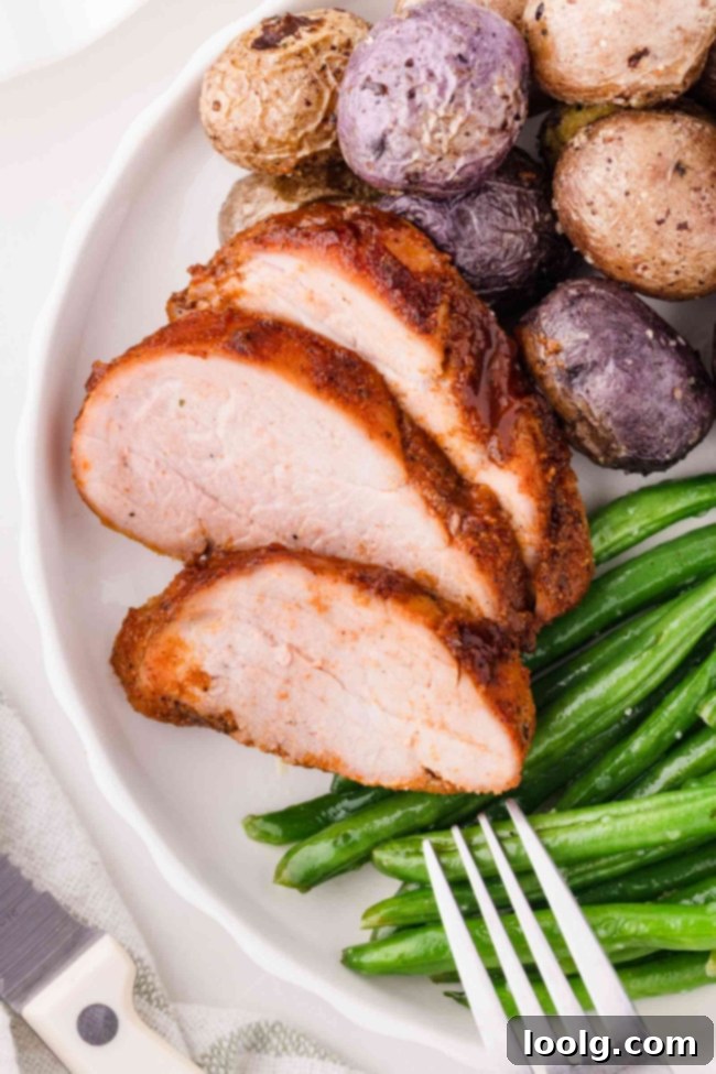 sliced pork tenderloin on white plate with beans and potatoes